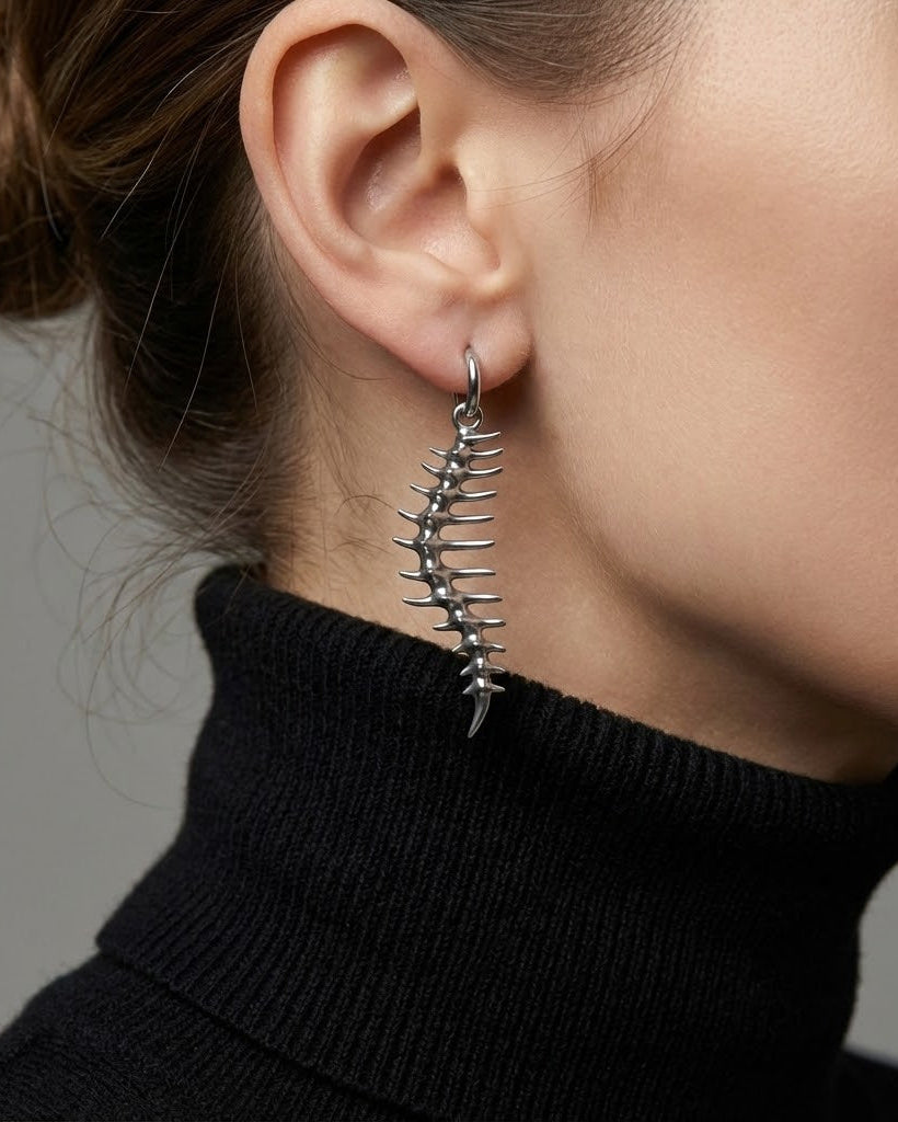 Close-up of a person wearing a unique silver earring with spikes against a neutral background