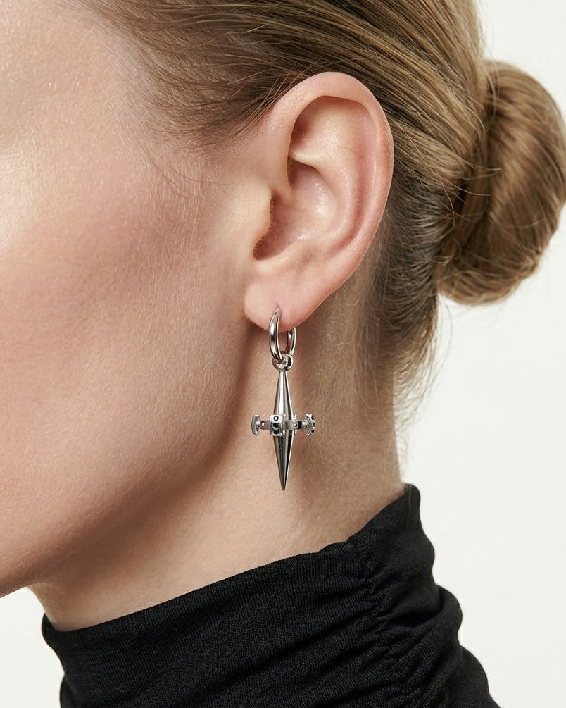 Close-up of a person wearing a silver earring with a pointed design on a neutral background