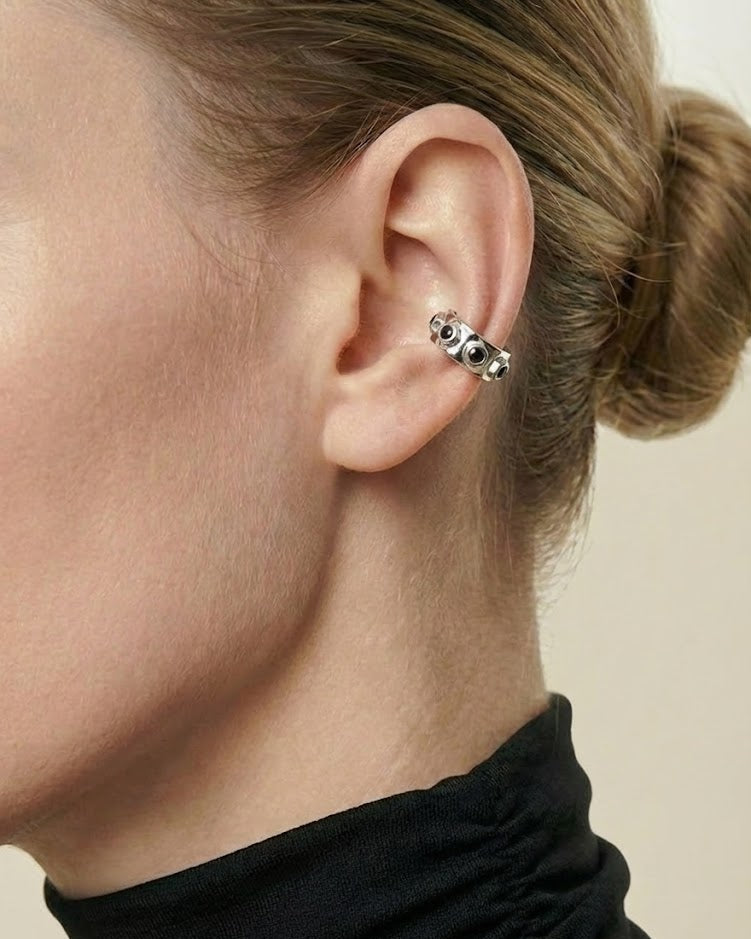 Close-up of an ear wearing a black and silver earring against a neutral background